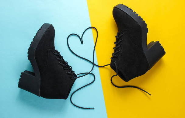 Black suede boots with heart-shaped laces on blue yellow background. Top view - 写真・画像