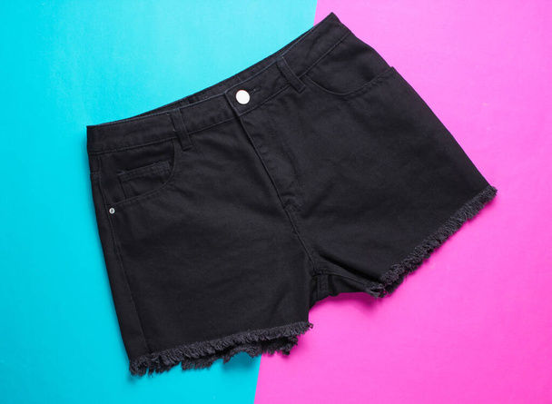 modische schwarze Jeans-Shorts auf rosa-blauem Hintergrund. Ansicht von oben. Minimalismus Modekonzept - Foto, Bild