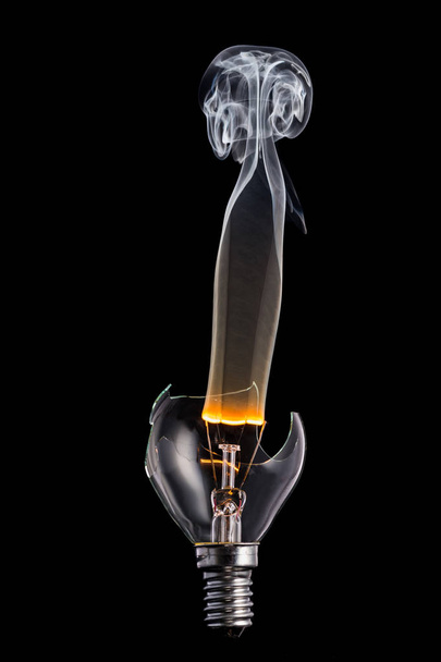 lâmpada quebrada e fumaça de uma espiral ardente em um fundo preto
 - Foto, Imagem