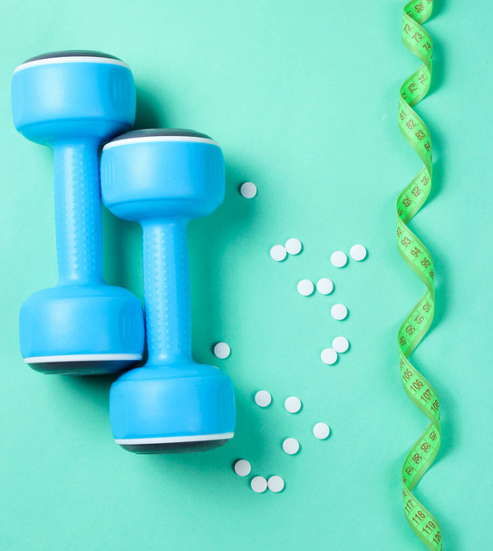 Sport weight loss concept. Dumbbells, ruler, pills on a blue background. Minimalism. Top view - Photo, Image