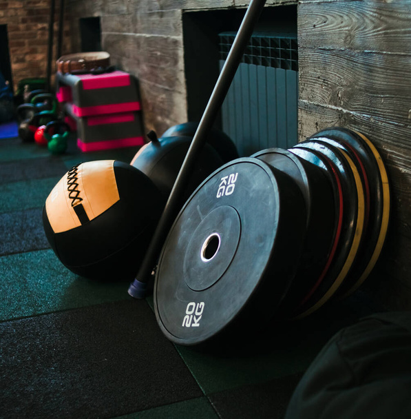 Équipement d'entraînement fonctionnel. Medicine ball, haltère, bâton de gymnastique sur le fond d'un mur en bois dans un gymnase sombre - Photo, image