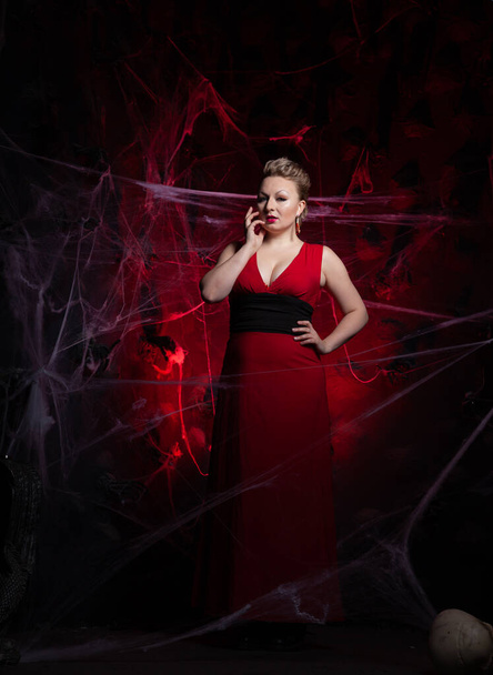 Woman in evening classic dress posing on black Halloween background with spider web - Фото, изображение