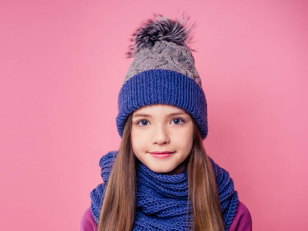 niedliches kleines Mädchen in warmer Strickmütze auf rosa Hintergrund in studio.children Winterkleidung - Foto, Bild