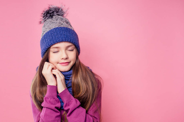 Beautiful little girl in winter warm colorful hat and scarf dreaming thought about the gift Christmas night in the studio on a pink background.portrait photography child model - Photo, image