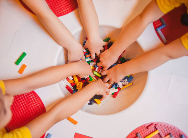 Vista superior das mãos de meninas brincando com tijolos de brinquedo na mesa no jardim de infância
 - Foto, Imagem