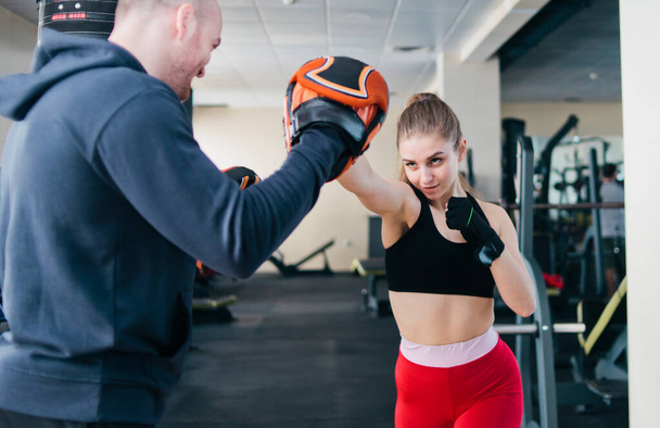 Mladá žena boxuje v tělocvičně s instruktorem. Pár cvičení punching - Fotografie, Obrázek