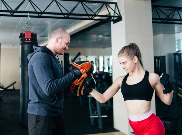 Přizpůsobivá blondýnka trénuje punč s trenérem. v tělocvičně. Pár cvičení punching - Fotografie, Obrázek