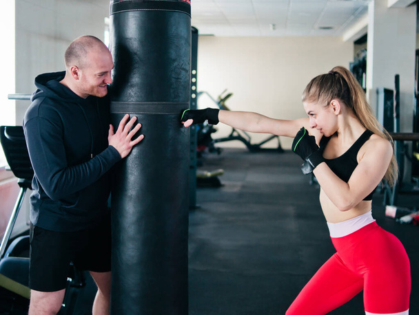 Инструктор-мужчина обучает молодую женщину делать удары руками в боксерской груше в спортзале. - Фото, изображение
