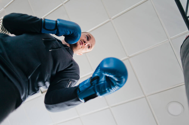 Man in bokshandschoenen boksen met een bokszak in de sportschool. Onderaanzicht - Foto, afbeelding
