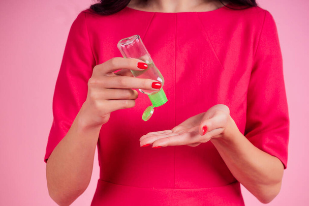 Woman hand applying hand sanitizer on a pink background in the studio - Foto, Imagen