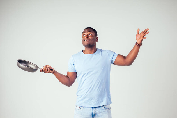 african american chef kitchener holding a frying pan wizard man cooking magic flying food salad, carrot, garlic, onion, pepper, potato, cucumber isolate white background studio.magic of taste fantasy - Fotó, kép