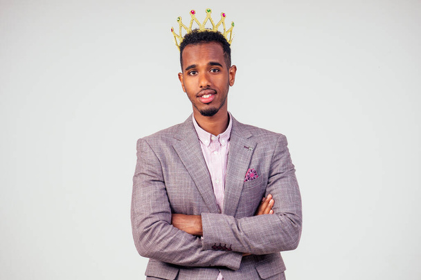 smart african american successful and rich businessman in a stylish suit and the golden crown on his head on white background in studio shot. the concept of well-deserved respect and luck - Фото, зображення