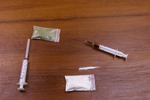 Different type of drugs: cocaine, heroin syringe and dried cannabis on a table. Drug use, crime and addiction concept - Photo, Image