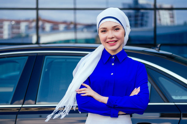 Arab business woman hijab standing in front of her luxury car on the street on a background of skyscrapers of Dubai. The woman is dressed in a stylish abaya - Foto, Imagen