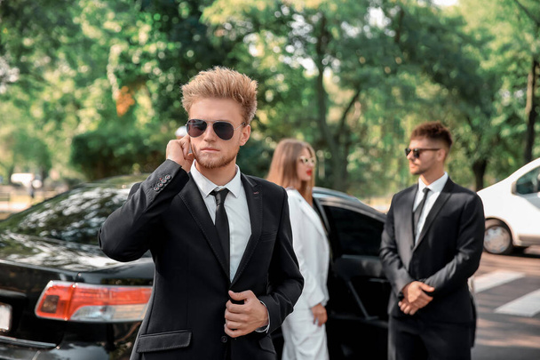 Jovem celebridade com guarda-costas perto do carro ao ar livre
 - Foto, Imagem