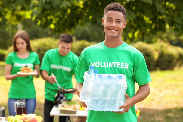 Jovem voluntário afro-americano com água para pessoas pobres ao ar livre
 - Foto, Imagem