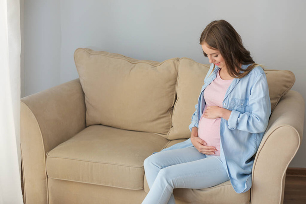Szép terhes nő ül a kanapén, otthon - Fotó, kép