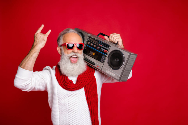 Portrait od foolish santa in eyewear eyeglasses holding boombox showing heavy metal sign wearing white pullover isolated over red background - Foto, imagen