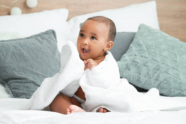 Lindo bebé afroamericano con toalla suave en la cama en casa
 - Foto, Imagen