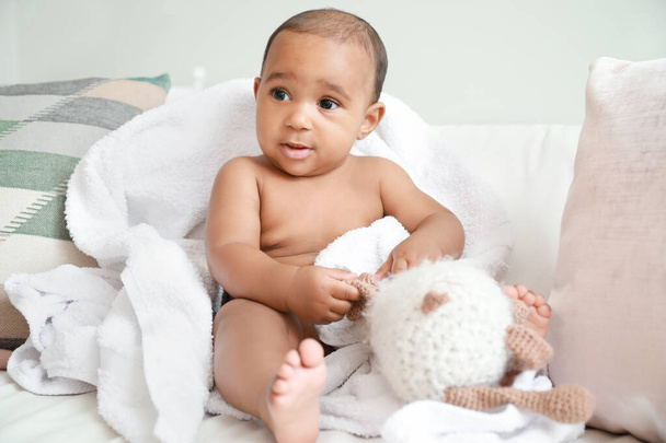 Schattige Afro-Amerikaanse baby met zachte handdoek en speelgoed op bed thuis - Foto, afbeelding