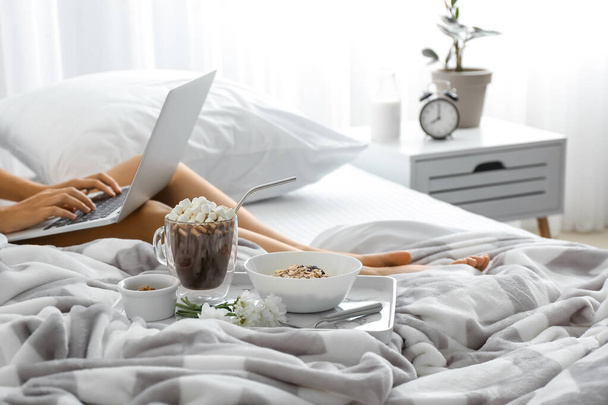 Młoda kobieta korzystająca z laptopa podczas śniadania w łóżku - Zdjęcie, obraz