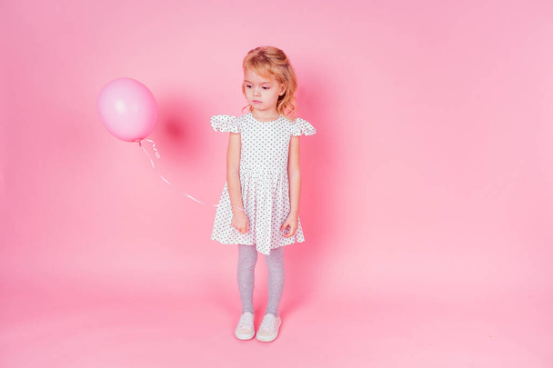 sad little blonde girl in white dress in peas 4-5 year old holding balloon in the studio on a pink background,birthday celebration ,sadness and disappointment sorrow - Foto, Imagen