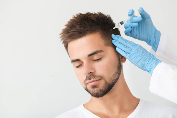 Man met haaruitval probleem met het krijgen van injectie op grijze achtergrond - Foto, afbeelding