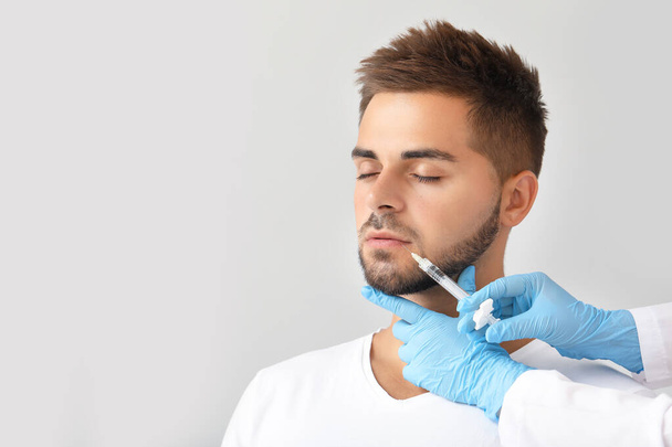 Handsome man receiving filler injection on grey background - Фото, зображення