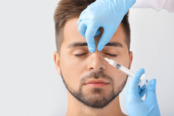 Handsome man receiving filler injection on grey background - Фото, изображение