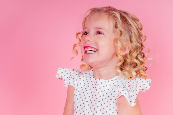 little girl beauty queen blue eyes, curls blonde hairstyle with a tiara crown on her head in a cute white dress in peas posing in the studio on a pink background.birthday celebration,Beauty contest - Photo, image