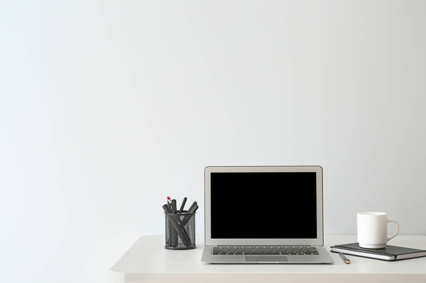Σύγχρονη χώρο εργασίας με φορητό υπολογιστή κοντά σε λευκό τοίχο - Φωτογραφία, εικόνα