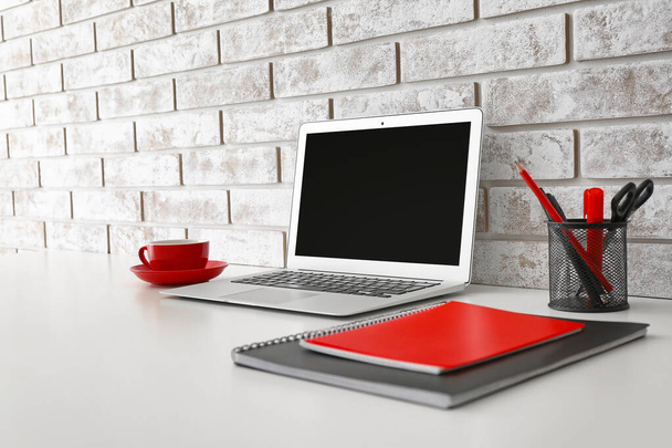 Modern munkahely laptop, írószer és csésze közelében téglafal - Fotó, kép
