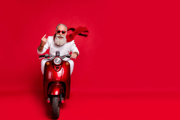 Full length photo of cheerful old man in eyewear eyeglasses showing rocker sign driving his bike wearing white sweater isolated over red background - Fotografie, Obrázek