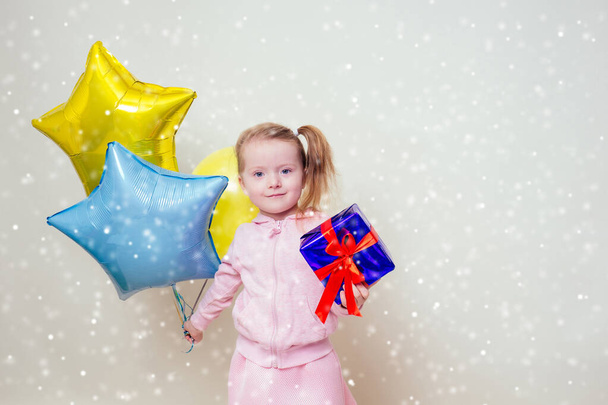 cute little girl holding helium blue, yellow and gold balloons and a box with a gift happy Birthday on white background in studio .christmas and new year holiday - Photo, Image