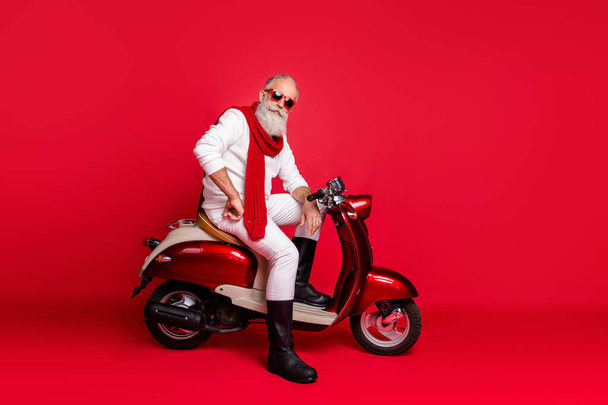Fancy grandfather santa man posing sitting on vintage moped wear jumper and trousers isolated red background - Photo, Image