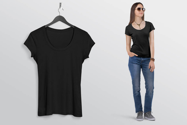 hängendes schwarzes einfaches kurzärmeliges T-Shirt an der Wand, mit schönem weiblichen Modell in blauer Jeanshose. isolierter Hintergrund. - Foto, Bild
