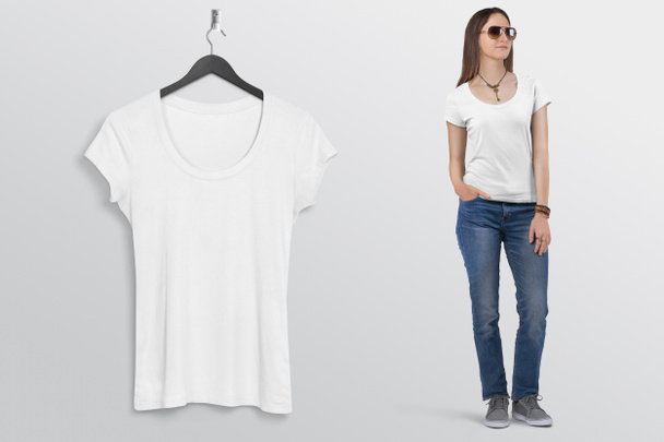 Maglietta bianca a maniche corte appesa a parete, con bellissimo modello femminile in jeans blu denim. Fondo isolato
. - Foto, immagini