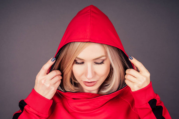 portrait of a beautiful blonde woman perfect skin and makeup put on hood hoodie sweatshirt red tracksuit sports suit hip hop dancer in studio on black background.Bob short hairstyle sensual style - Photo, image