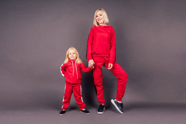 full length portrait mother with the daughter in sports suits.beautiful young blonde woman with a little girl posing in red stylish suit studio black background,active sporting family hip-hop dancer - Foto, afbeelding