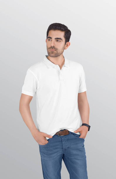 Крупный план стоящего мужчины-модели в белой футболке из поло в джинсах в голубой джинсе. Изолированный фон
. - Фото, изображение