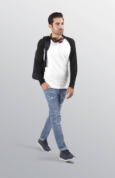 Caminante modelo masculino con camisa de manga larga raglán liso blanco y negro en pantalón vaquero desgarrado azul. Con una mochila negra en el hombro. Fondo aislado
 - Foto, imagen