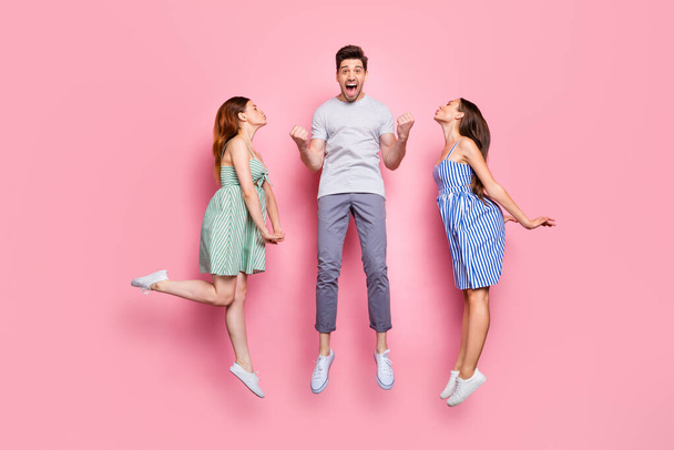 Full size profile side photo of screaming person with raised fists and charming ladies kissing him wearing striped t-shirt pants isolated over pink background - Foto, Imagen