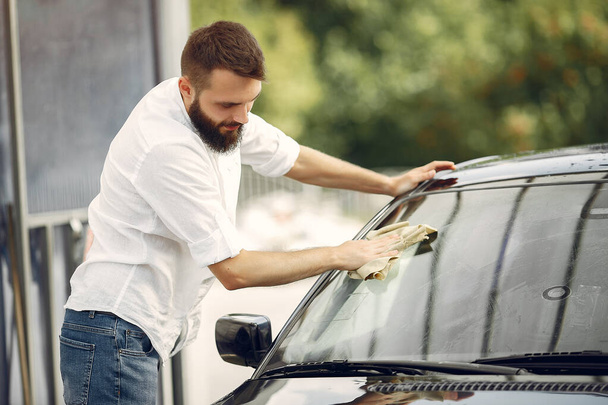Man in a white shirt wipes a car in a car wash - Фото, зображення