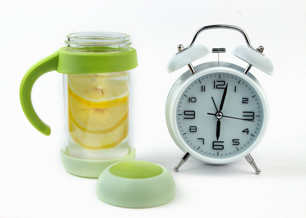 Çalar saat ve cam bir masada limon ile bir detoks bardak su. Sabah alarmı ile erken kalkın. - Fotoğraf, Görsel