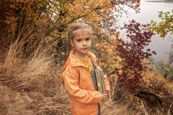 Slim schattig kind meisje met een boek met droge gele bladeren - Foto, afbeelding