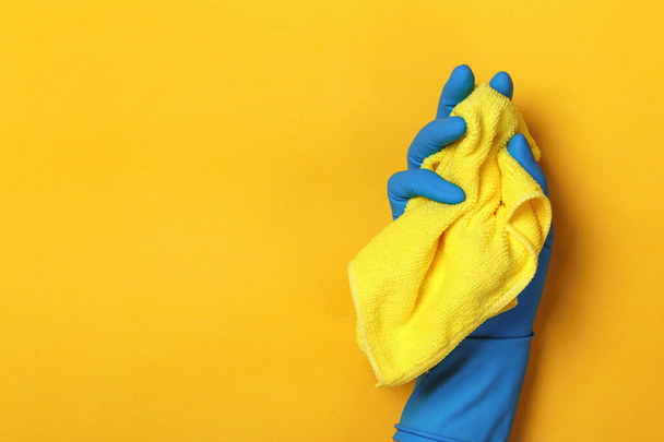 A hand in a protective blue glove holds a yellow rag on a yellow colored background - Foto, Imagen