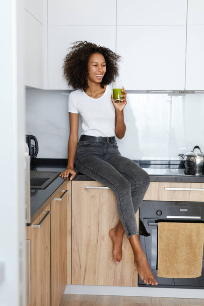 Woman drinking green detox juice, smoothie drink in kitchen - Fotó, kép
