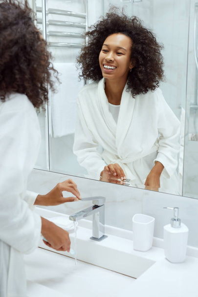 Woman with smile and beauty face looking in mirror at bathroom - Photo, Image