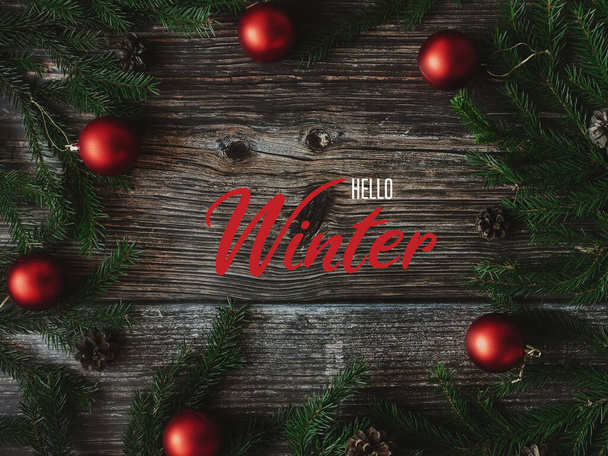 επιγραφή Γεια σας Χειμώνας σε ξύλινο φόντο με κλαδιά ελάτης και κόκκινες μπάλες - Φωτογραφία, εικόνα
