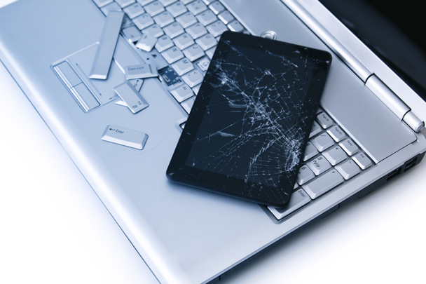A silver laptop with a broken keyboard, tablet with a cracked display. A close-up picture of part of broken laptop and cracked screen on a tablet. - Foto, Imagen